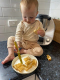 Child sitting on kitchen counter using child safe knife to cut toast.